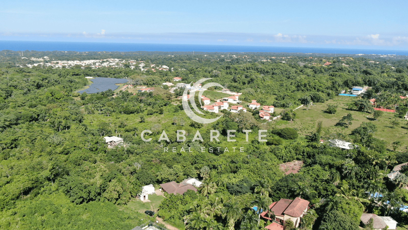 Clear, flat land plot for sale in a secure gated community, with a few palm trees and blue skies above.