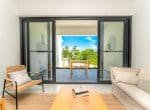 Modern living room with sliding glass doors leading to a balcony with outdoor seating and a view of a tropical garden.