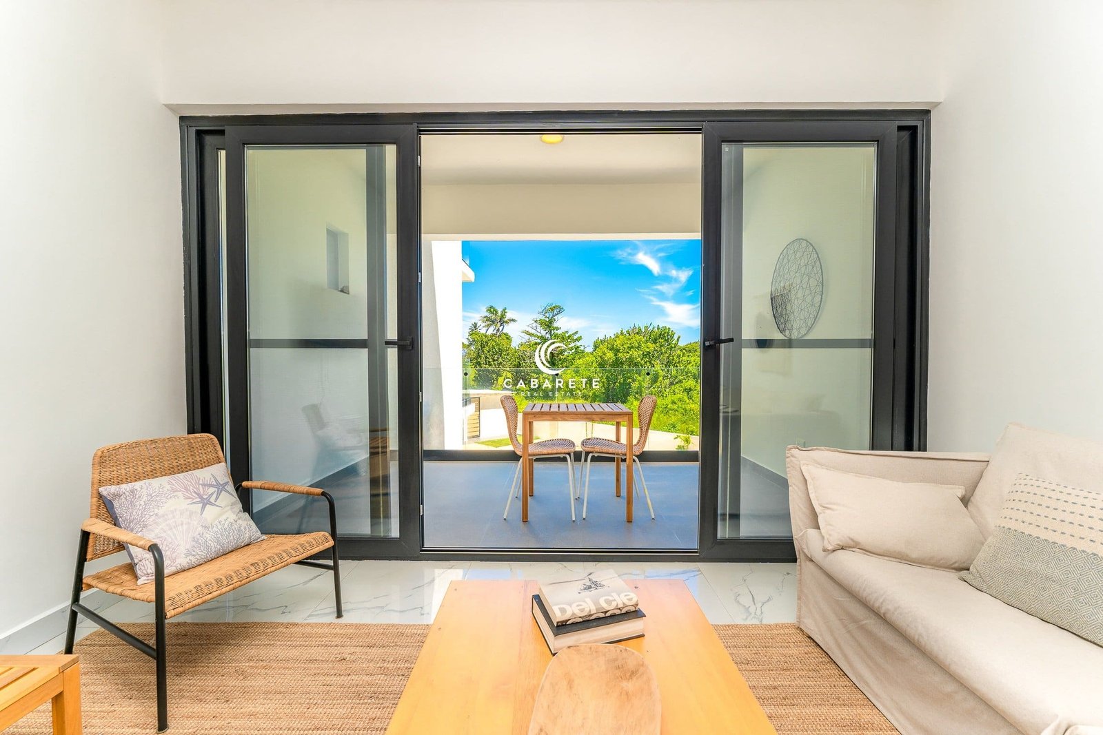 Moderno salón con puertas correderas de cristal que dan a un balcón con asientos al aire libre y vistas a un jardín tropical.