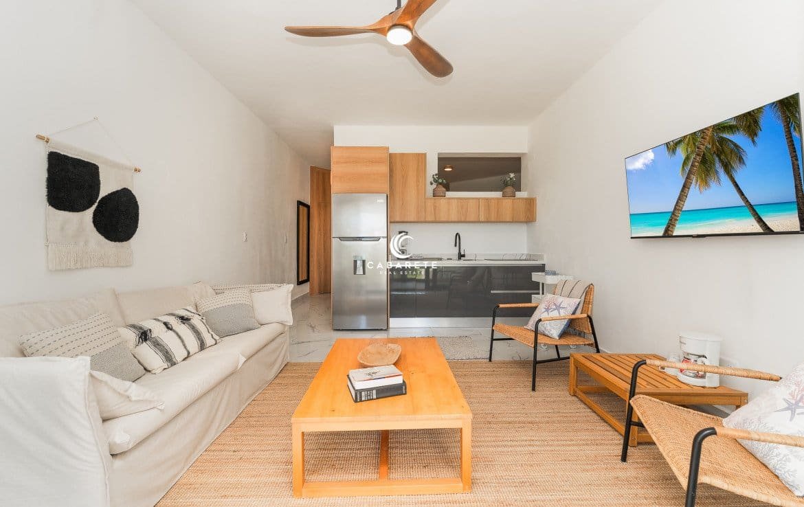 Modern living room with comfortable seating, a ceiling fan, a television, and an open kitchen.