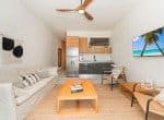Modern living room with comfortable seating, a ceiling fan, a television, and an open kitchen.