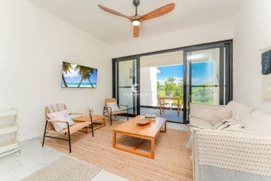 Modernes Wohnzimmer mit bequemen Sitzgelegenheiten, einem Deckenventilator und Glasschiebetüren, die auf einen Balkon führen.